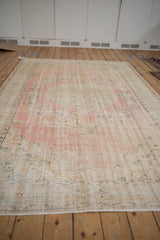 Distressed Oushak rug showing worn texture in soft rose, ivory, and green.