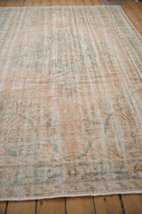 Vintage distressed Oushak rug, low pile texture with faded dusty blush and green motifs.