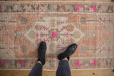 Blush and fuchsia floral motifs on a distressed vintage Oushak rug, with foundation showing.