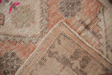 Distressed Oushak rug corner showing dusty blush pile, visible foundation weave, and original selvage.
