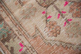 Distressed Oushak rug texture showing low pile, fuchsia, dusty blush, and pale green motifs.