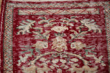 Distressed cherry red Oushak rug texture revealing floral motifs and light foundation.