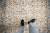 Distressed vintage Turkish Sparta rug with feet on faded ivory, blue, pink floral vinery, showing wear.