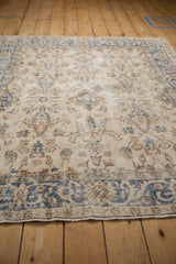 Distressed Sparta rug detail showing faded ivory pile, blue vines, pink motifs, and visible foundation.