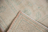 Close-up of Turkish Oushak rug's distressed texture, secured edge, and visible woven foundation.