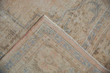 Distressed Oushak rug corner showing worn pile, exposed foundation, and a border with subtle blue and rose tones.