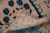 Distressed pink Oushak rug pile texture with blue motifs, showing secured edge and woven foundation.