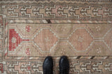 Worn beige and dusty rose Oushak runner, showcasing pinwheel floral motifs and geometric border.