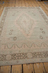 Distressed Oushak rug featuring soft seafoam green, dusty rose medallion, and worn texture.