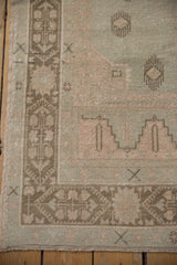 Distressed vintage Oushak rug corner: pale seafoam field, finned floral motifs, geometric dusty bronze border.