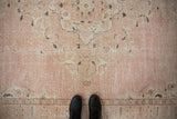 Distressed pink and ivory vintage Sparta rug, showing worn pile, subtle patterns, and dark boots.