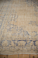 Distressed Oushak rug showing worn knot heads, cobalt blue scrolling floral patterns on light beige.