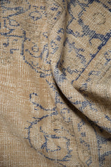Close-up of distressed Oushak carpet with worn beige pile and faded cobalt blue patterns.
