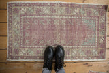 Vintage distressed Oushak rug in purple and mint green, shown on a wood floor for scale.
