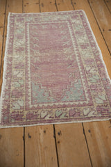 Angled view of a distressed Oushak rug showing its soft pile in purple, ivory, and mint green.