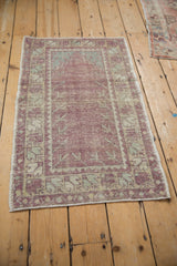 Angled view of a distressed Oushak rug with a purple prayer design and mint green border.