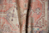 A draped view highlighting the distressed texture and muted blush tones of the vintage rug.