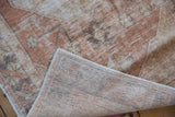 Folded corner of a distressed Oushak rug showing the hand-knotted weave and worn pile texture.