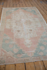 Distressed vintage Oushak rug corner, showcasing wear, coral, ivory, and dusty teal patterns.