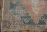 Distressed Oushak rug corner, geometric border, worn coral and dusty teal pile, intact selvage.