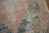 Distressed Oushak rug with faded coral, dusty teal geometric pattern, and visible foundation wear.