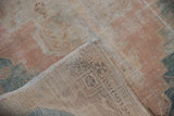 Vintage distressed Oushak rug folded corner with worn coral pile and woven backing.