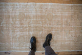 Distressed Oushak runner texture, faded medallions, exposed foundation, dusty gold.