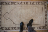 Worn texture and prayer format design of a distressed beige Oushak rug.