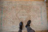 Distressed Oushak rug displaying even wear, low pile, and faded turquoise-mauve patterns.