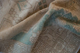 Softly folded vintage Oushak rug showing low pile texture in sand and pale turquoise.