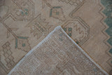 Folded corner of a distressed Oushak rug showing the low pile and hand-knotted reverse.
