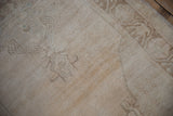 Close-up of distressed ivory Oushak runner pile with faded curvilinear motifs in cream and pale brown.
