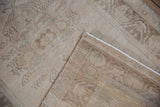 Distressed Oushak rug corner revealing woven foundation, side selvage, ivory and pale coffee tones.