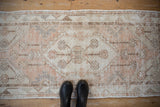 Distressed vintage Oushak runner showcasing worn floral medallion in ivory, dusty melon, and beige.