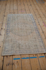 Angled view of the distressed Oushak rug, highlighting the heavily worn pile and faded medallion.