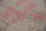 Distressed Oushak pile showing faded raspberry, ivory, and seafoam green tones.