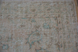 Distressed vintage Turkish Oushak rug corner, cream, coffee, and seafoam hues, visible foundation.