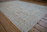 Decorative distressed Oushak rug corner, displaying worn texture and soft cream and green tones.