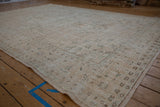 Distressed Oushak carpet corner, showing worn cream and seafoam green blossom motifs.