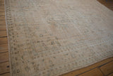 Distressed cream and coffee brown Oushak rug corner showing faded green geometric border.