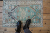 Worn mint green and beige distressed Oushak rug, showing soft pile and patterns with boots.