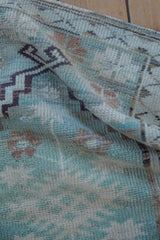 Folded distressed Oushak rug with textured abrashes, mint green, beige, and dark geometric motif.