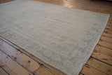 Vintage Distressed Oushak rug corner, low pile ivory with faded teal floral border details.