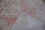 Texture of distressed Oushak rug pile in dusty blush, beige, and ivory, with hand-knotted back.
