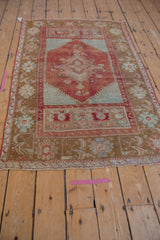 Distressed Anatolian rug: arabesque floral border, cherry red field, turquoise, aubergine spandrels.