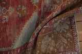 Folded vintage distressed Anatolian rug pile revealing cherry red and turquoise mint blossom patterns.