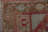 Distressed Anatolian rug corner: cherry red arabesque border, bronze field, turquoise accents, even wear.