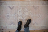 Distressed Oushak runner's pale mauve medallion, ivory tones, and worn texture underfoot.
