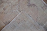 Distressed vintage Oushak rug with worn pile, hand-knotted foundation, and intact selvage.
