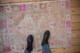 Distressed vintage Oushak rug with worn pile, hot pink, ivory, and sand tones, underfoot.